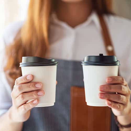 A waitress holding and serving two paper cups of hot coffee in cafe