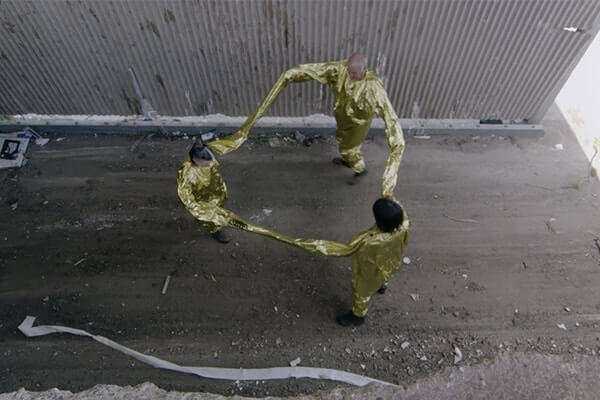 Three people in gold costumes hold hands, part of Kyneton (triadic transfer) by Eugenia Lim in the Okkoota ಒಕ್ಕೂಟ program.