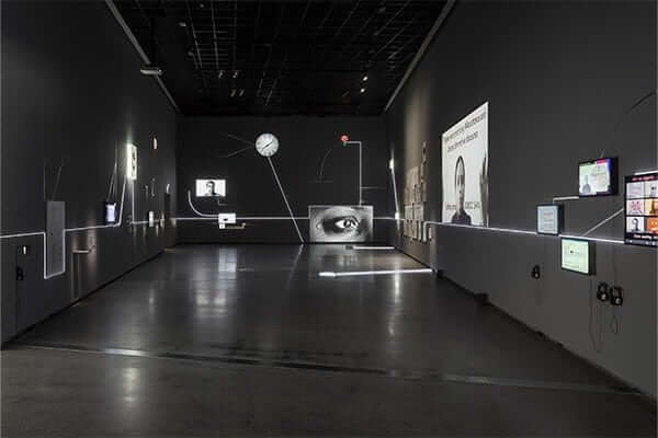 A wide angle view of the main exhibition room. A dark room with lots of projections and a continuous led strip. 