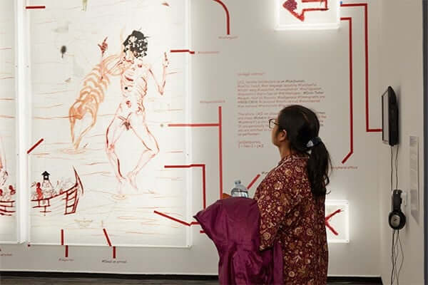 A woman stands and looks at a Mithu Sen piece, a graphic, skeletal sketch with lots of red lines on the sides. 
