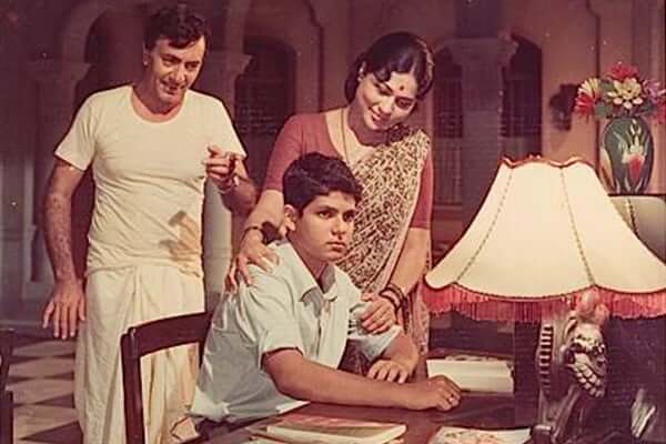 Old Bollywood movie depicts a boy sitting at a table whilst his family watch him.