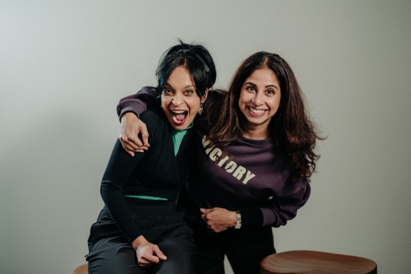 Deepa Mani puts an arm over Sheena Chundee's shoulder. They are both smiling.