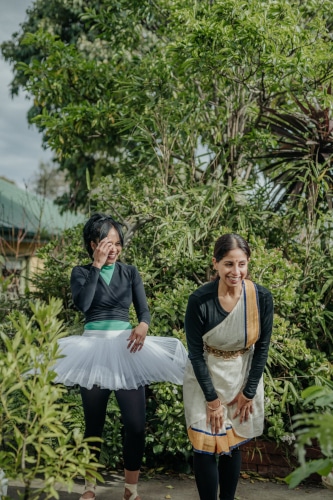 Sheena Chundee in a tutu and Deepa Mani in traditional clothing, pose for a photo in a garden.
