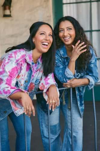 Yasmin and Menik wearing denim clothing. They smile whilst looking off into the distance. 