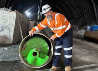 A man stands with a large green drill piece.