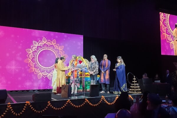 People on stage exchanging gifts in traditional Indian costumes. 