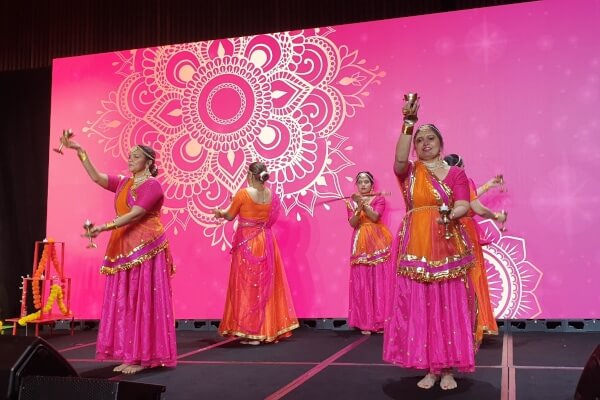 Dancers dressed in orange and pink clothes dance on stage.