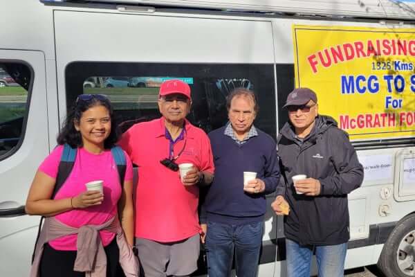 Four people stand in front of a white van, holding cup of chai. 
