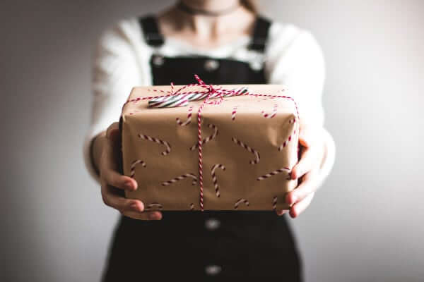 A woman in black overalls holds out a gift wrapped in brown paper with candy canes stamps on it.