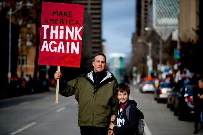 Man beside boy holding rally sign in Seattle, United States in 2017 ahead of US election
